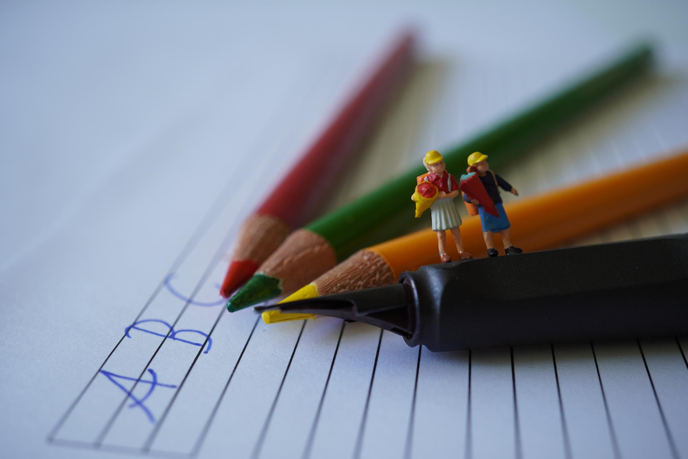 Buntstifte auf denen 2 Kinderfiguren mit Schultüten stehen