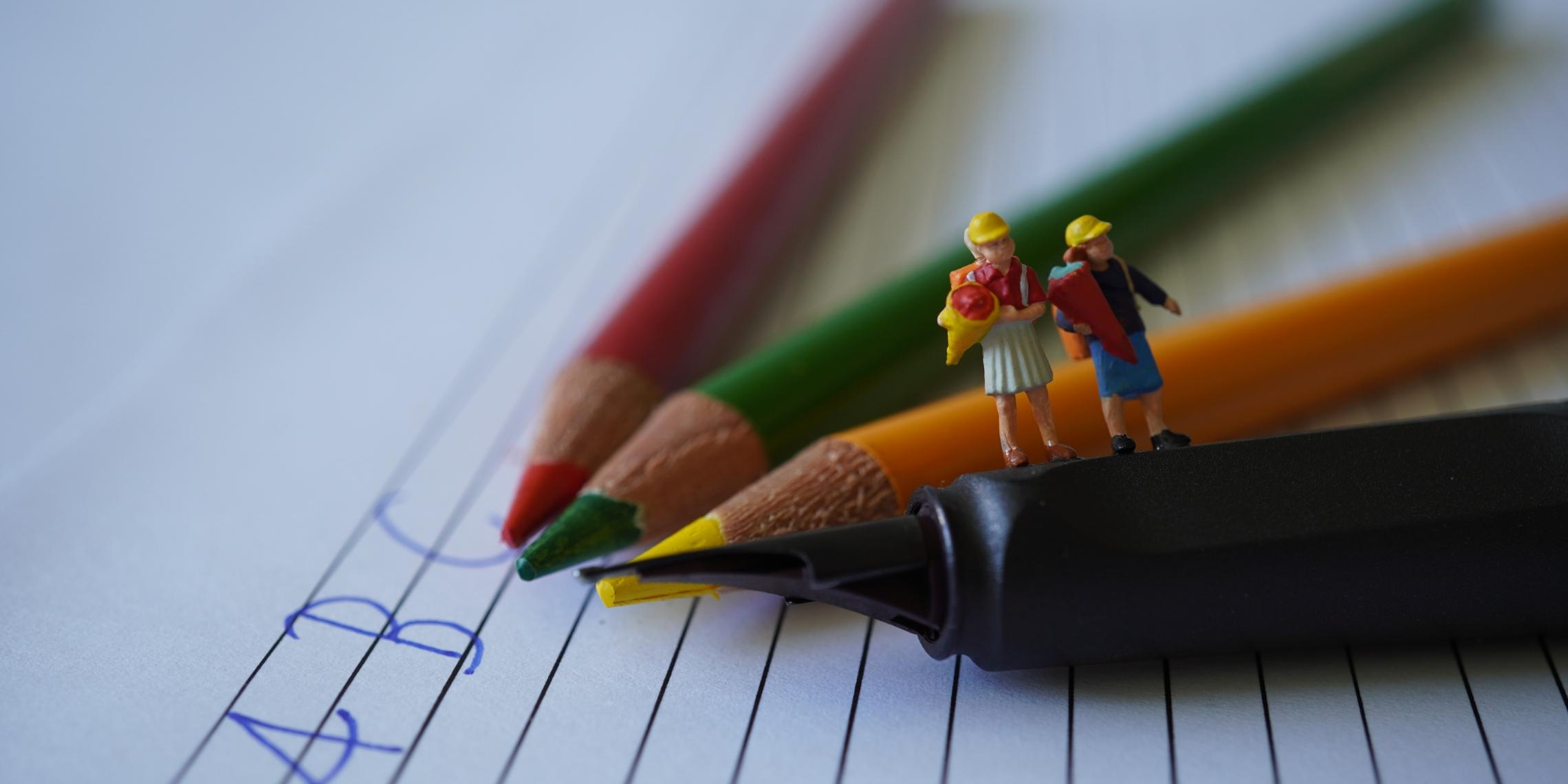 Buntstifte auf denen 2 Kinderfiguren mit Schultüten stehen