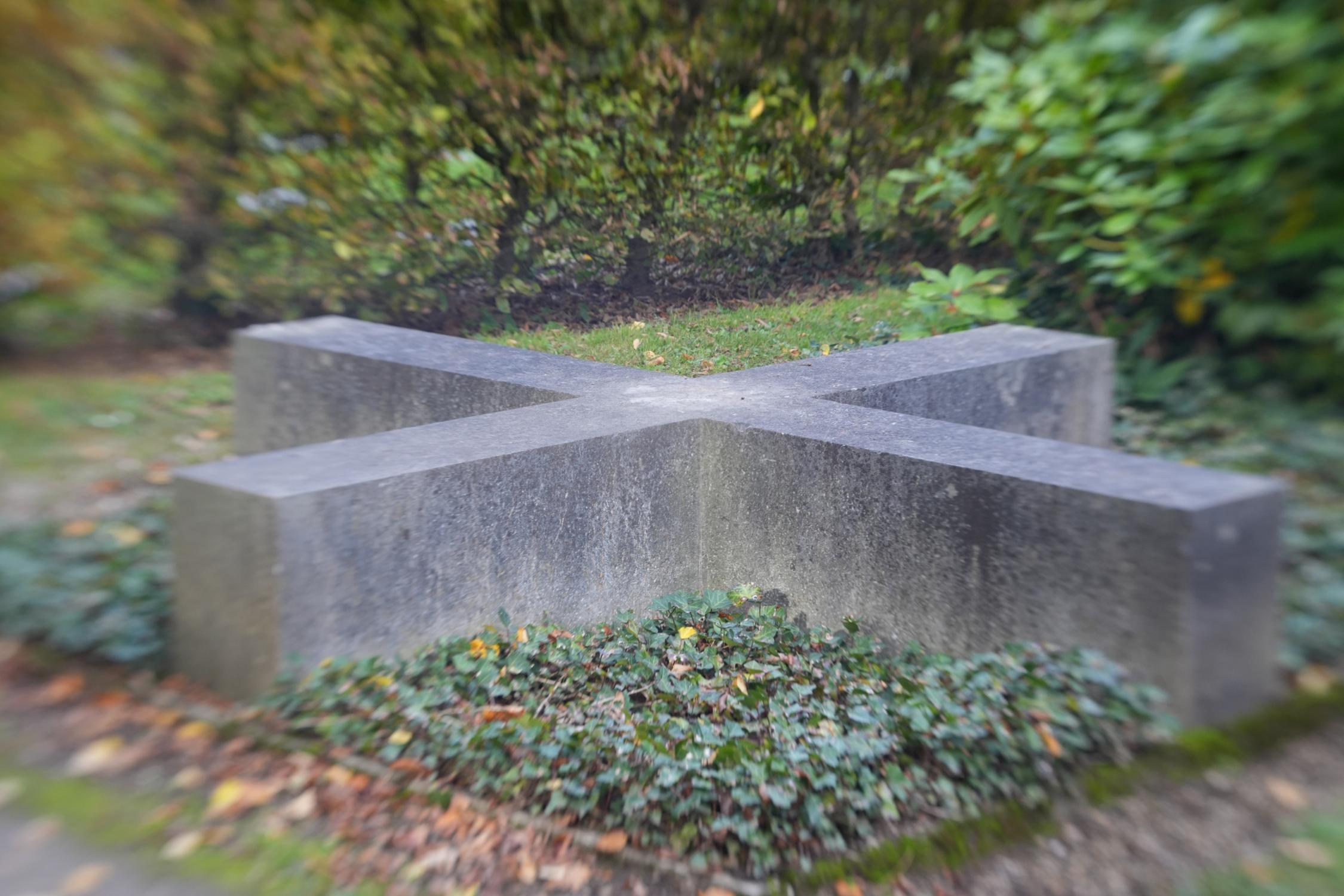 auf dem Boden liegender Gedenkstein in Form eines Kreuzes aus Granit auf einer Efeufläche