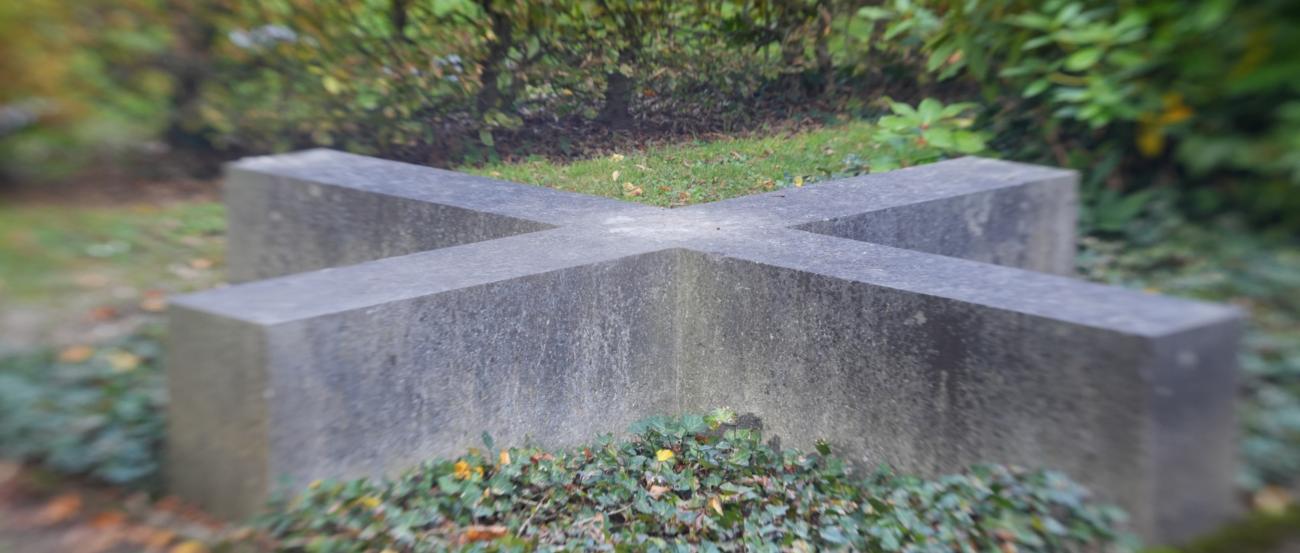 Friedhof Heerdt (c) Beatrix Reese auf dem Boden liegender Gedenkstein in Form eines Kreuzes aus Granit auf einer Efeufläche
