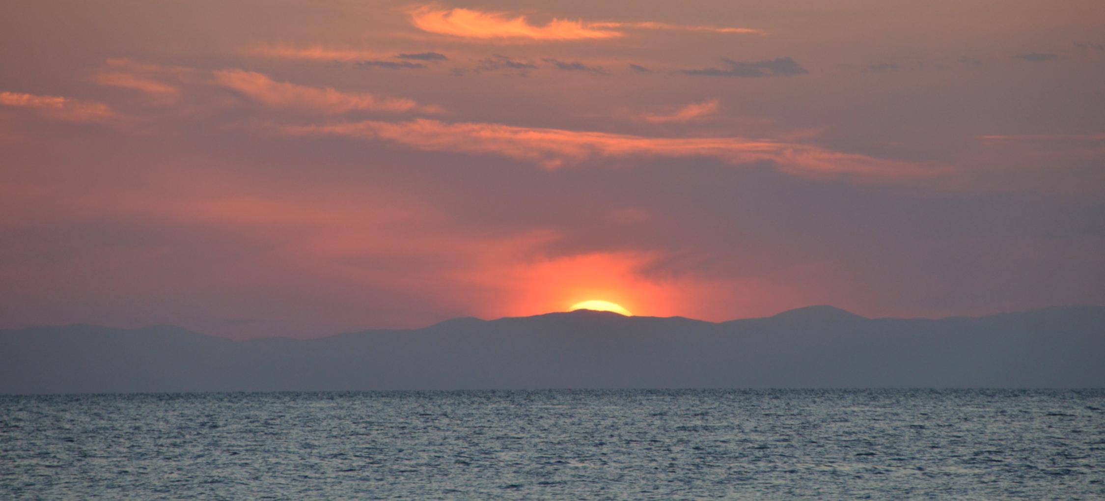 Sonne kurz vor dem Untergang hinter eine Wolke über dem Meer am Horizont