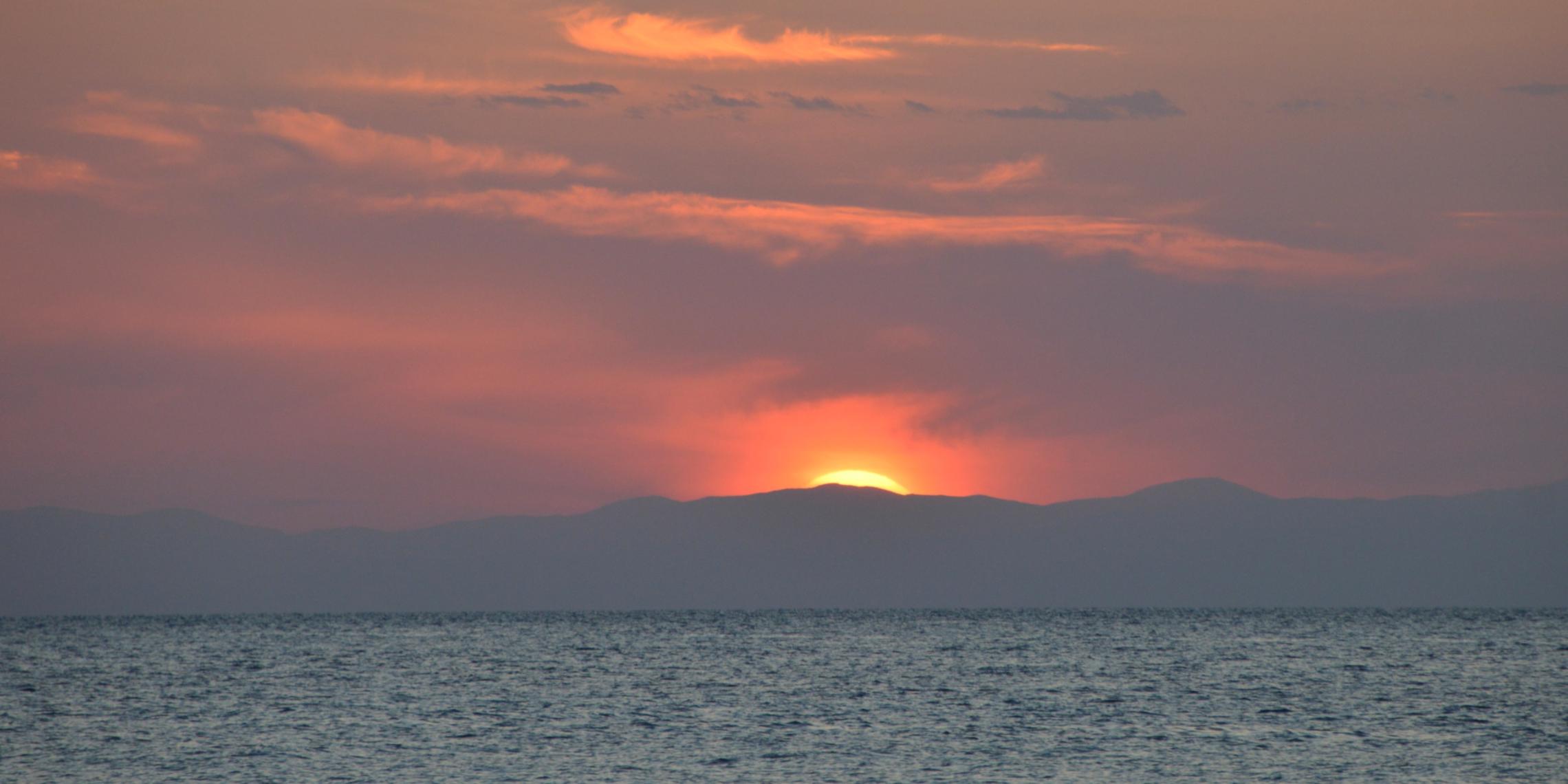 Sonne kurz vor dem Untergang hinter eine Wolke über dem Meer am Horizont