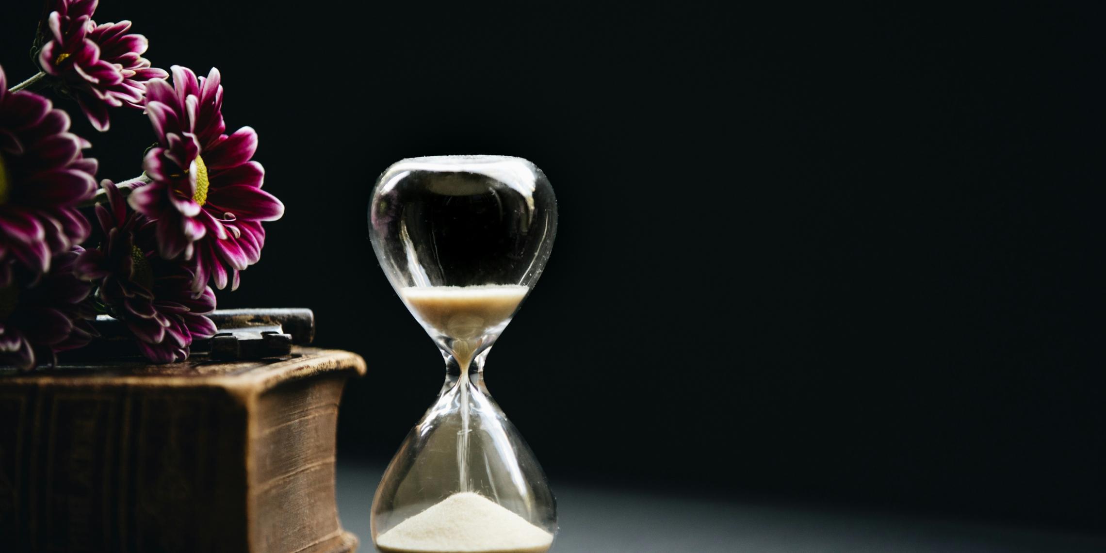 Sanduhr neben Buch mit Blumen