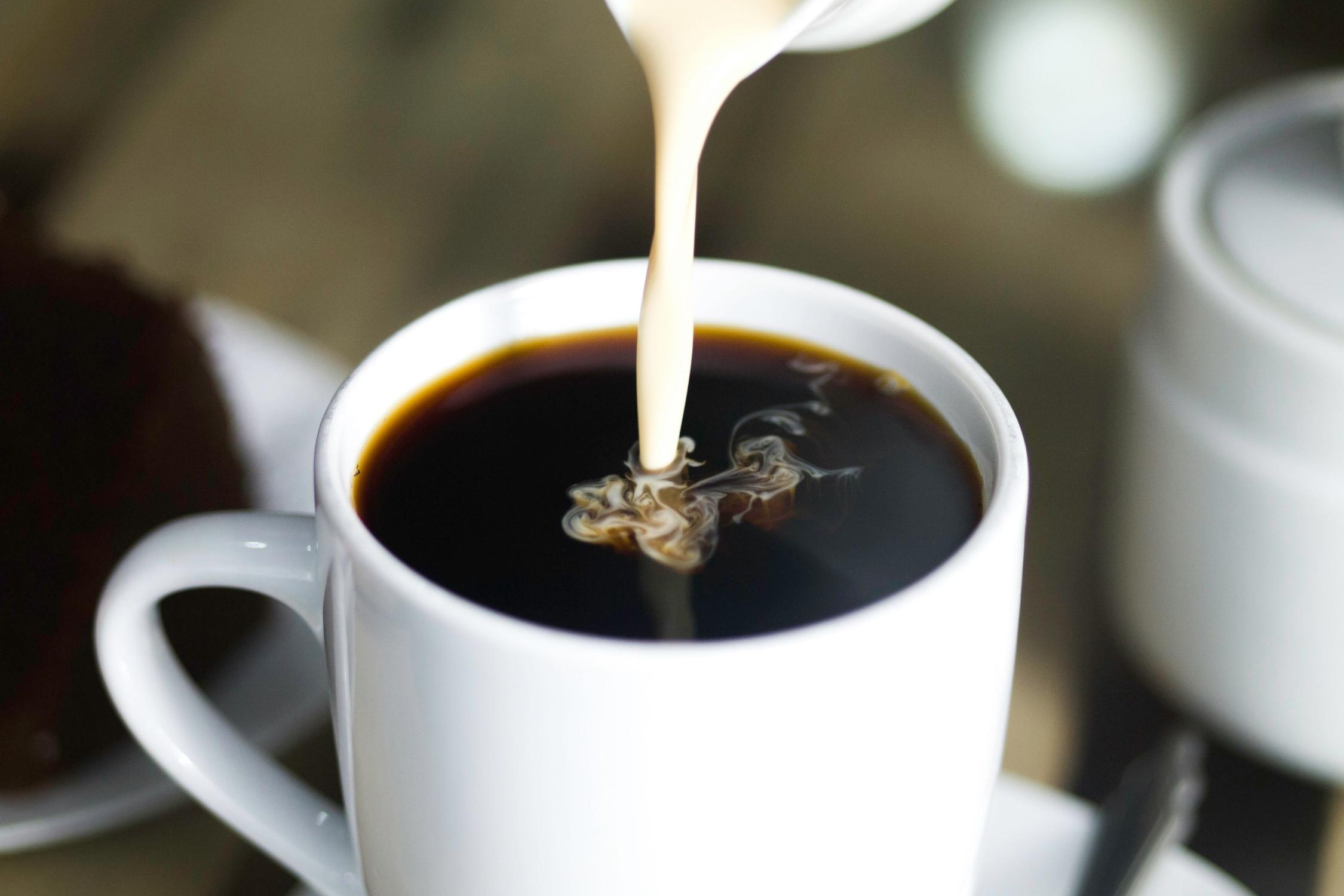 Milch wird in eine Kaffeetasse gegossen