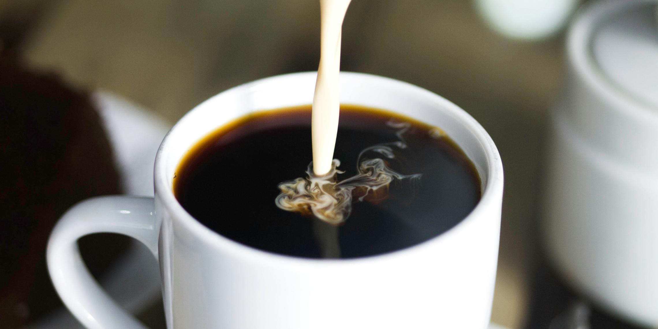 Milch wird in eine Kaffeetasse gegossen